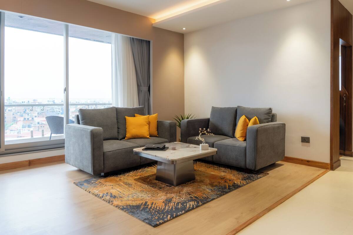 Una sala de estar moderna con dos sofás grises, una mesa de centro y un amplio ventanal con cortinas.