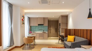 Ein modernes Hotelzimmer mit Bett, Sofa, Esstisch mit Stühlen, Küchenzeile und Bad.