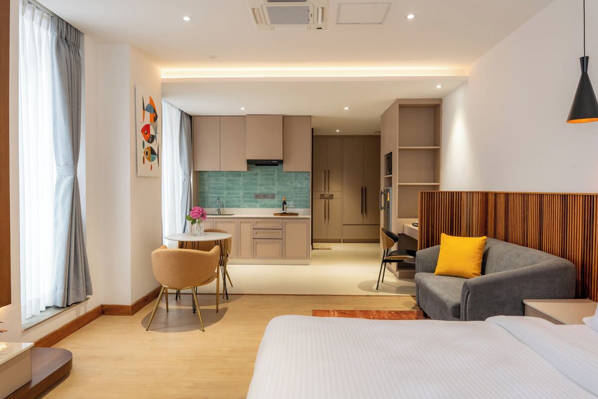 Una habitación de hotel moderna con cama, sofá, mesa de comedor con sillas, zona de cocina y baño.
