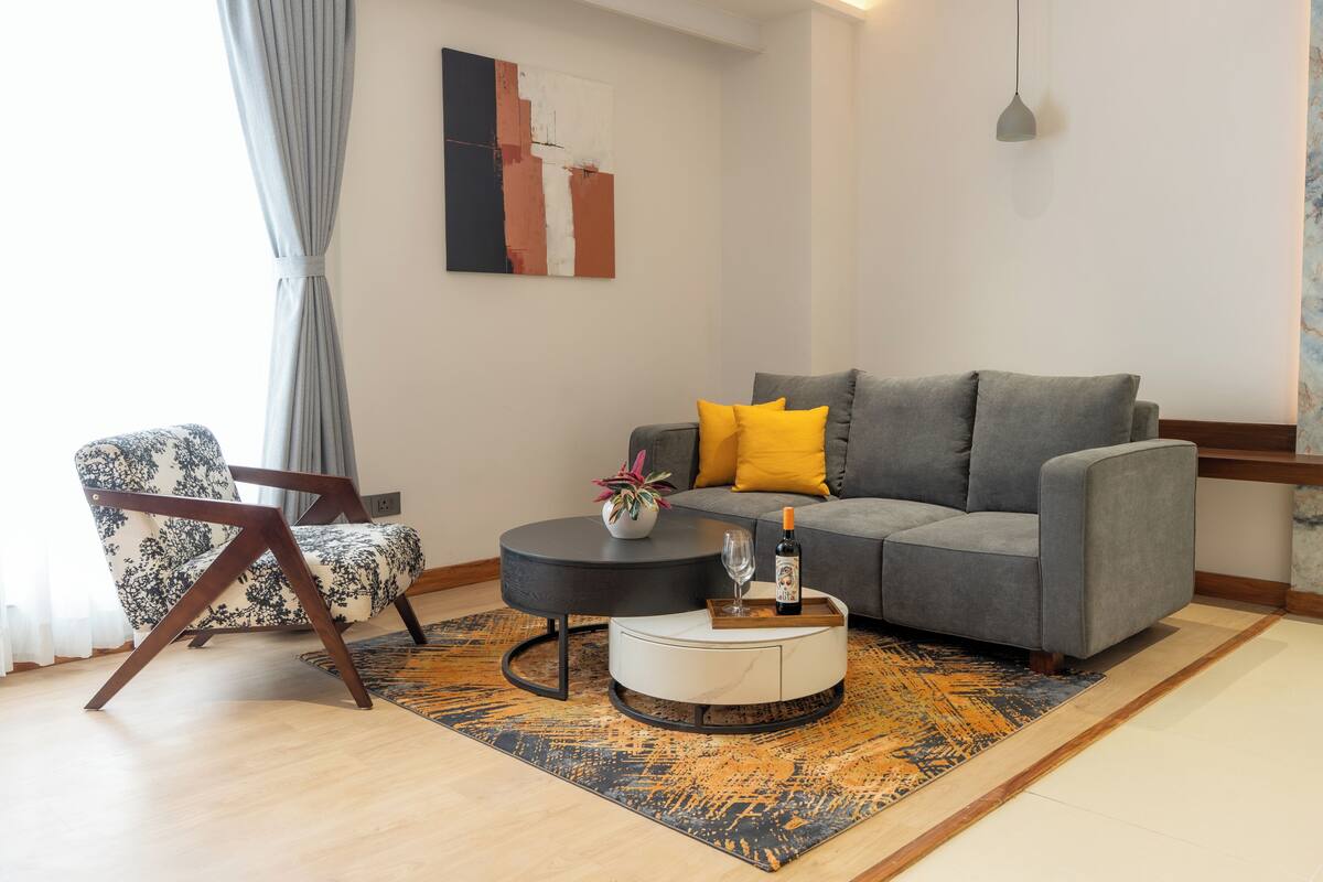 Una sala moderna con un sofá gris, un sillón estampado, una mesa de centro redonda y un jarrón decorativo.