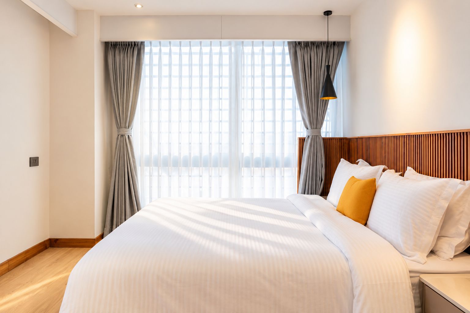 A hotel room with a large bed, a wooden headboard, and a view through the window.