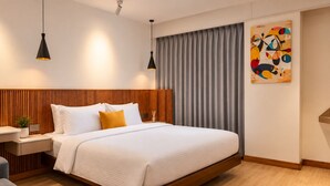 A modern hotel room with a large bed, wooden headboard, bedside tables, a desk, and a painting on the wall. - Maya Suites (Lalitpur)