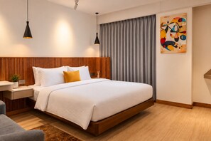 Una habitación de hotel moderna con una cama grande, cabecera de madera, mesitas de noche, un escritorio y un cuadro en la pared.