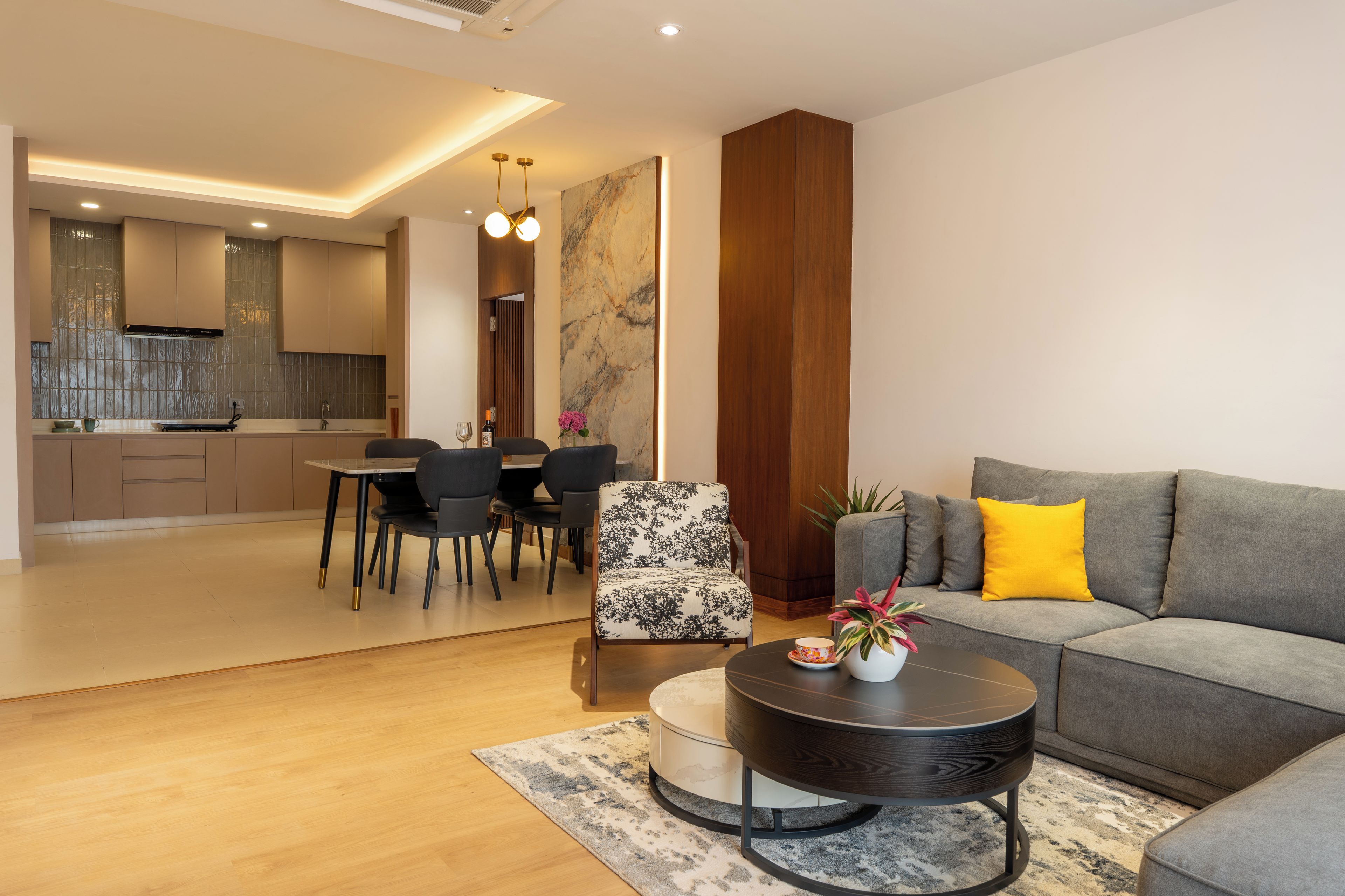 Ein modernes Wohnzimmer mit einem grauen Sofa, einem gemusterten Sessel und einem runden Couchtisch.