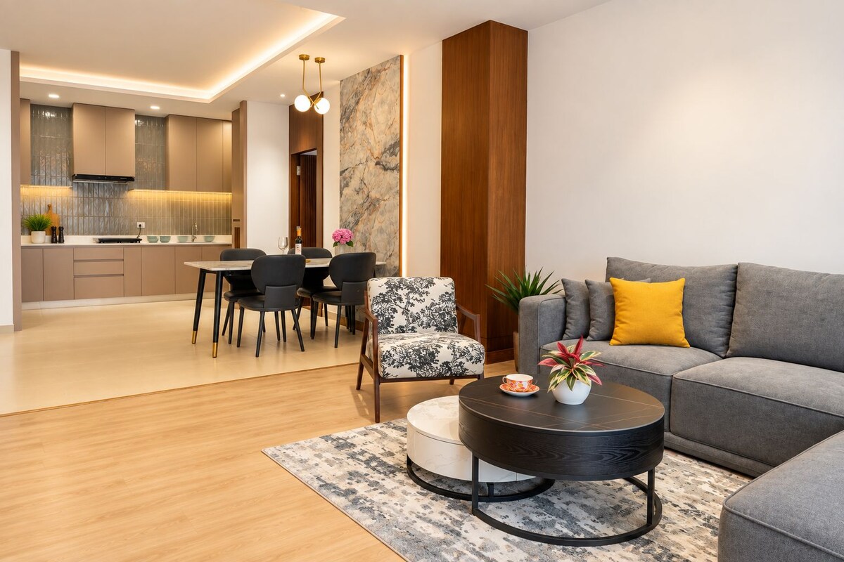 Una sala de estar moderna con un sofá gris, un sillón estampado, una mesita de centro y un comedor con mesa y sillas.