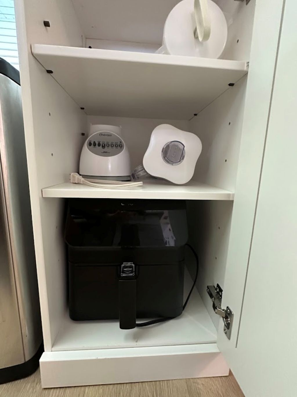 Un gabinete blanco con una licuadora, un recipiente blanco y un caja de almacenamiento negra.
