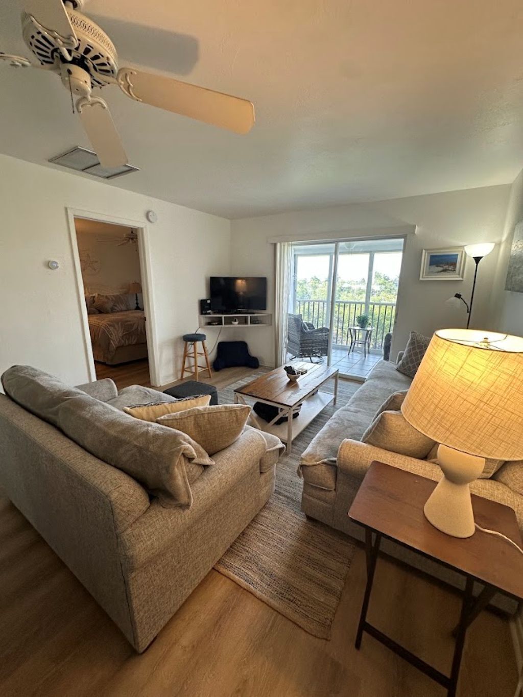 Una sala de estar con sofá, mesa de centro, lámpara, televisor y balcón con vistas.