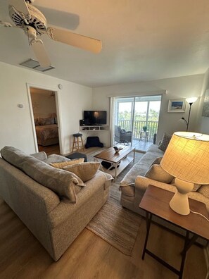 Ein Wohnzimmer mit Sofa, Couchtisch, Lampe, Fernseher und einem Balkon mit Blick.