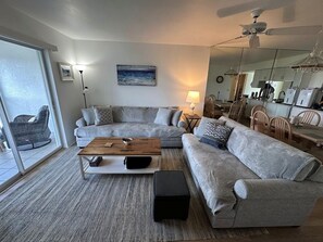 En stue med en hjørnesofa, et sofabord, en lampe og et spiseområde med stole og et bord.