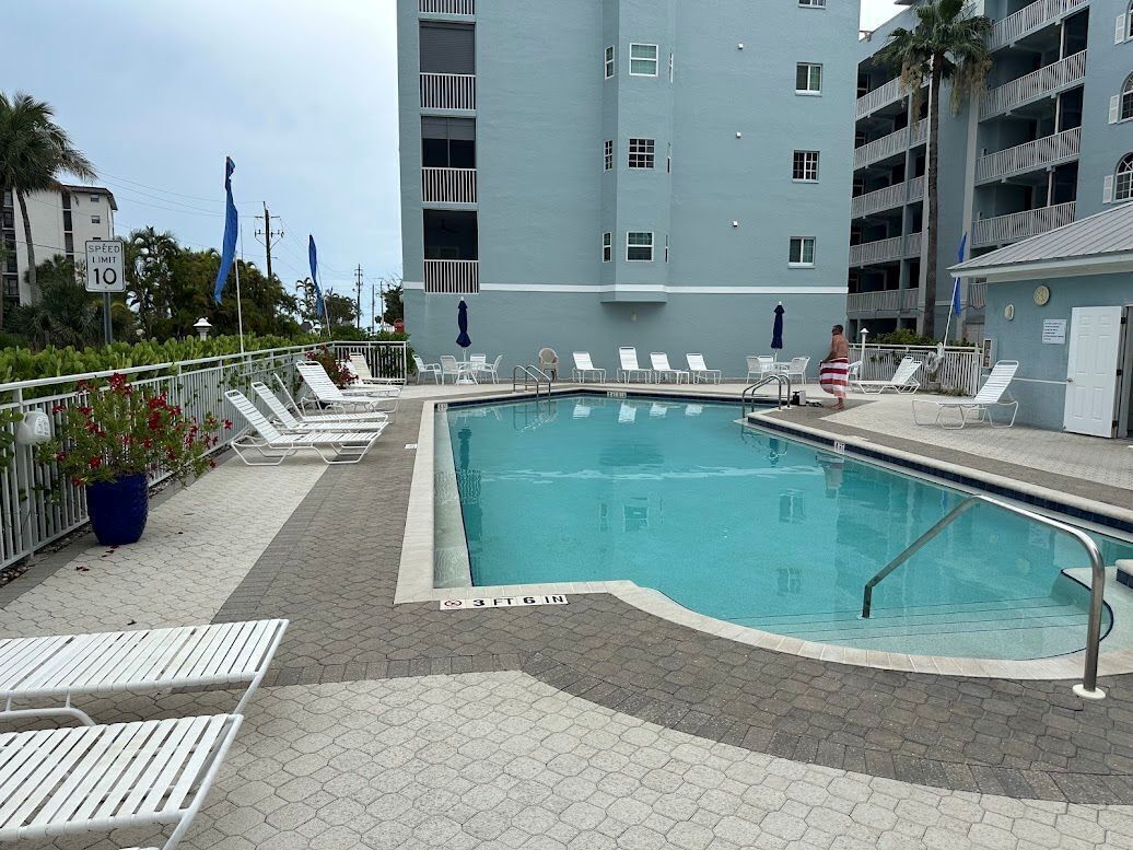 A swimming pool with lounge chairs, a speed limit sign, and a multi-story building in the background.