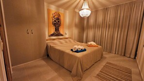 Une chambre d’hôtel avec un lit, un lustre, un tableau et une fenêtre avec des rideaux.