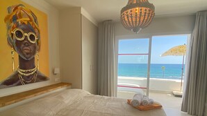Ett hotellrum med en stor säng, en tavla på väggen, en kristallkrona och utsikt över havet.