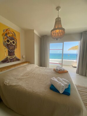 Ein Hotelzimmer mit einem großen Bett, einem Gemälde an der Wand, einer Chandelüster und Blick auf den Ozean.