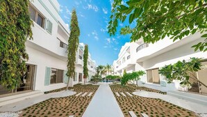 Un patio central con un sendero, rodeado de edificios blancos con balcones y vegetación.