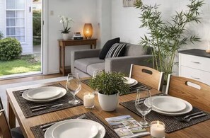 A dining table set with plates, cutlery, and candles, surrounded by chairs, with a sofa and a plant in the background. - Spacious 4-bed Retreat in Vibrant Footscray (Melbourne)