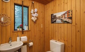 Un baño con paneles de madera, un lavamanos, un inodoro y una ventana con vistas a la calle.