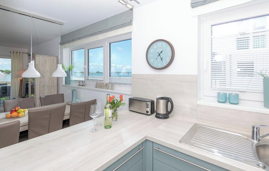 A modern kitchen with a large window, a clock, a toaster, a kettle, and a sink.