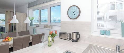 A modern kitchen with a large window, a clock, a toaster, a kettle, and a sink.