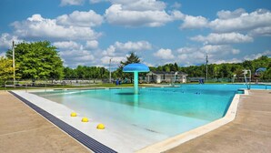 Ein Swimmingpool mit blauem Sonnensegel, umgeben von einer Betonplattform und einem Rasenbereich.