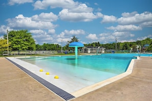 Ein Swimmingpool mit blauem Sonnensegel, umgeben von einer Betonplattform und einem Rasenbereich.