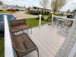 A deck with wicker chairs, a small table, and a view of a residential area with houses and parked cars. - Tattershall Lakes - Hot Tub - Sleeps 6 - Pets (Lincoln)