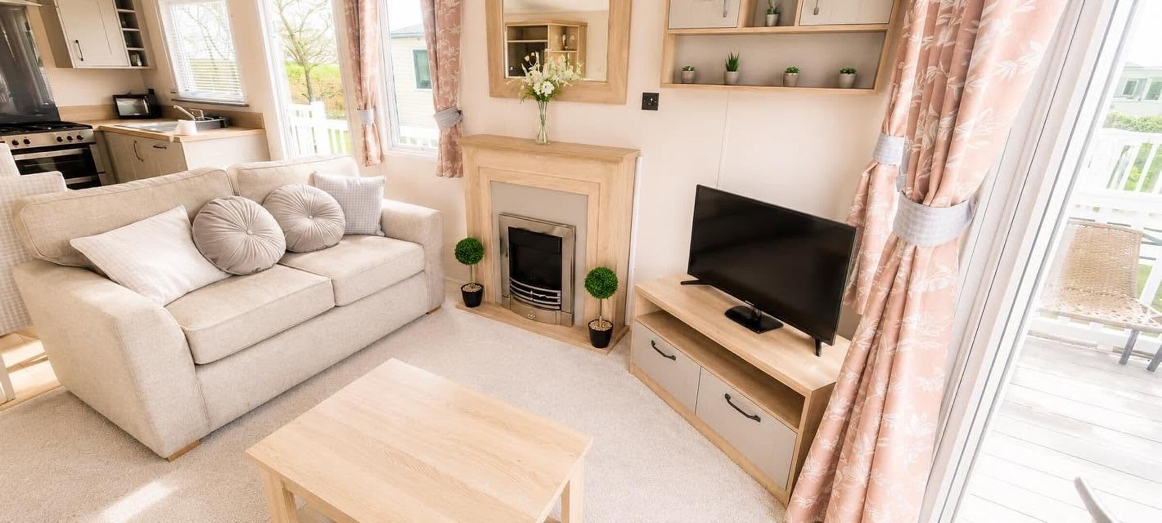 A living room with a sofa, TV, fireplace, and a kitchen area visible in the background.