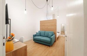 Een kamer met een blauwgroene bank, houten vloer, een bureau met een bloevas en een houten scheidingswand.