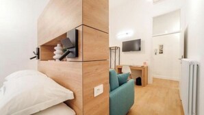Ein modernes Zimmer mit einem Bett, einem türkisfarbenen Sofa, einem Fernseher und einem Schreibtisch mit einer Lampe.