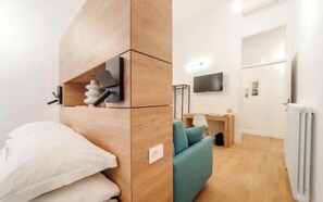 Ein modernes Zimmer mit einem Bett, einem türkisfarbenen Sofa, einem Fernseher und einem Schreibtisch mit einer Lampe.