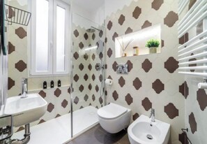Een badkamer met een douche, twee wastafels, een toilet en een spiegel.