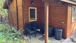A wooden cabin with a covered porch, two windows, and outdoor seating. - Hidden in the forest - cozy vacation home for quiet days in nature (Wittingen)