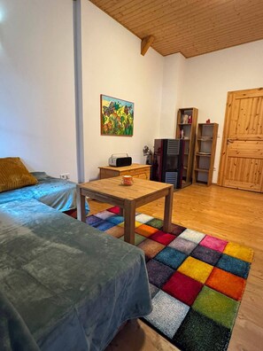 A room with a bed, a table, a colorful rug, a bookshelf, and a door.