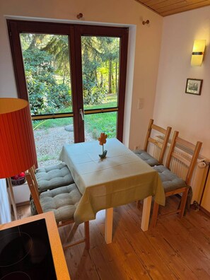 A dining area with a table set for two, a bench, and a view of a garden through a glass door. - Hidden in the forest - cozy vacation home for quiet days in nature (Wittingen)