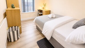 Ein Schlafzimmer mit Bett, Schreibtisch, Stuhl, einem Fenster mit Vorhängen, einer Heizung und einem Stauraum.