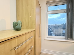 A room with a wooden cabinet, a window with a view of a residential street, and a cactus on the cabinet. - The Shed - Cosy 2-Bed Flat with Free Parking - Close to City Centre (Cardiff)