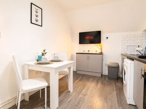 A compact kitchen with a dining area, a washing machine, and a TV mounted above the counter. - The Shed - Cosy 2-Bed Flat with Free Parking - Close to City Centre (Cardiff)