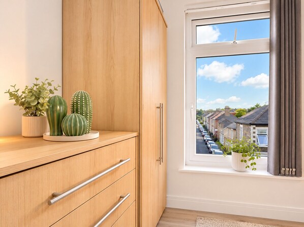 A room with a wooden cabinet, a window with curtains, and a view of a residential street. - The Shed - Cosy 2-Bed Flat with Free Parking - Close to City Centre (Cardiff)