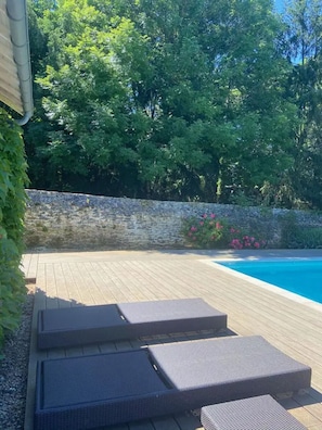 Une terrasse en bois avec des chaises longues, un mur en pierre et une piscine.
