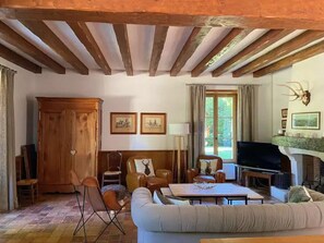 Un salon comprenant un canapé, des fauteuils, un téléviseur, une cheminée et un plafond en bois.