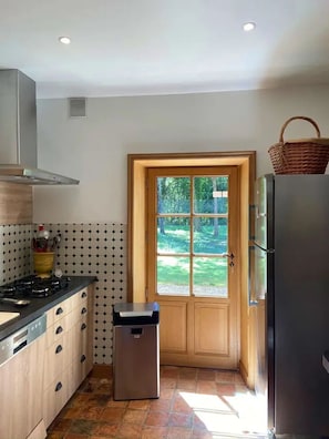 Une cuisine équipée d’un fourneau, de placards, d’une poubelle, d’un réfrigérateur et d’une porte donnant sur l’extérieur.