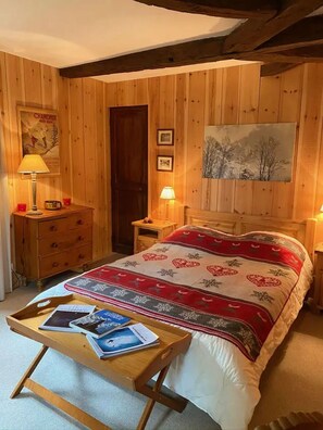Une pièce aux murs lambrissés, comprenant un lit, une table de chevet, une commode et une lampe.