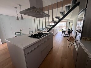 Eine moderne Küche mit einer zentralen Kochinsel, ein Essbereich mit Tisch und Stühlen sowie eine Treppe, die in eine obere Ebene führt.