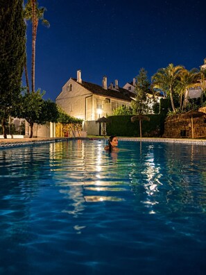 A swimming pool with a person in the water, surrounded by palm trees and a building with a tiled roof. - Marbella Golden Mile Townhouse 4 bedrooms, Saltwater Pools & Walk to the Beach (Marbella)
