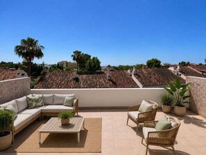 Eine Dachterrasse mit einer Couch, Stühlen, einem Tisch und Topfpflanzen.