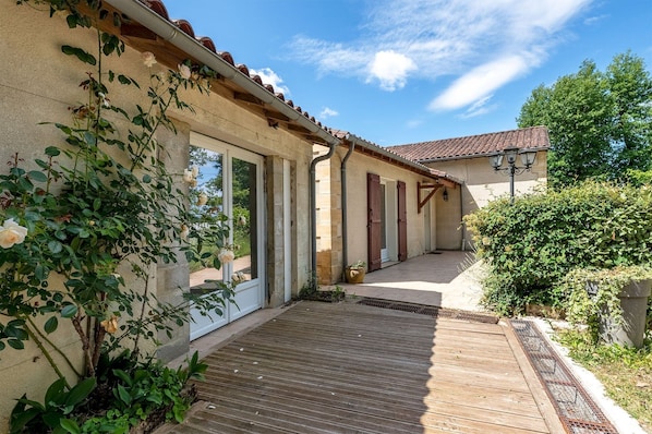 A building with a wooden deck, a garden with roses, and a clear sky.