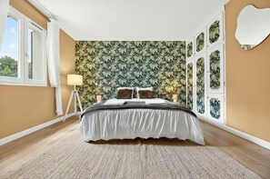 Une chambre à coucher avec un papier peint à motifs, un lit avec une literie blanche, une lampe sur pied et une fenêtre avec des rideaux.