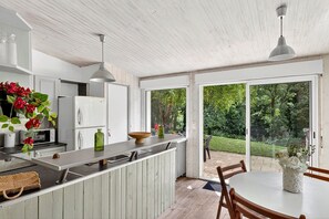 Une cuisine moderne avec un plafond en bois, des armoires blanches et une grande porte-fenêtre coulissante donnant sur un jardin.