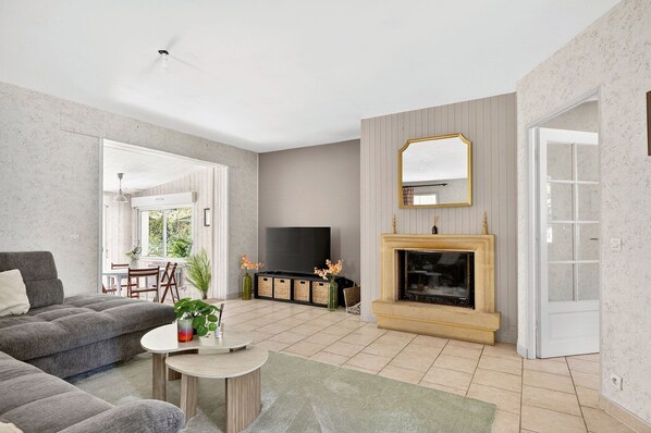 A living room with a sofa, a TV, a fireplace, and a dining area with chairs and a table.