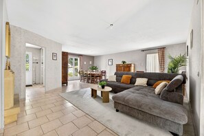 A living room with a sectional sofa, a dining area, and a staircase leading to another level.