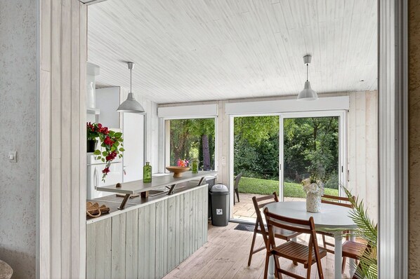 Une terrasse couverte avec une table et des chaises, un comptoir de cuisine avec un évier et une poubelle.